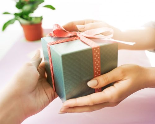 close-up-female-hands-holding-present-trendy-pink-desk_155003-6784